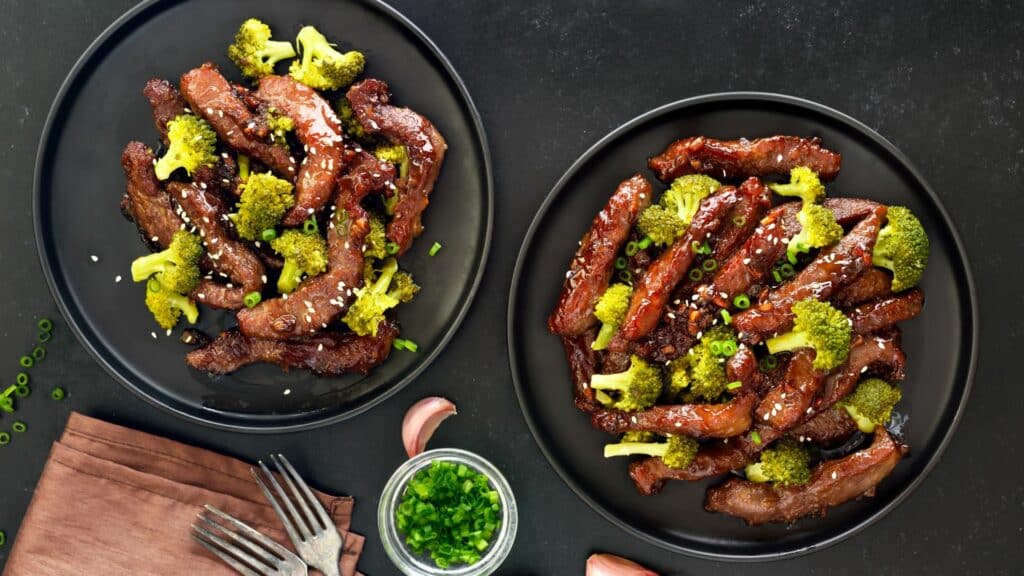 Beef and broccoli stir-fry on black plates.