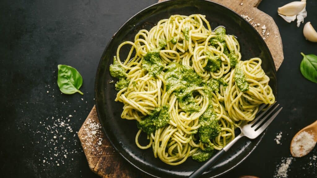 Spaghetti with pesto sauce on black plate.