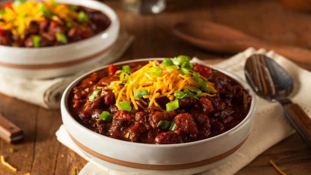 Bowl of chili with cheese and green onions.