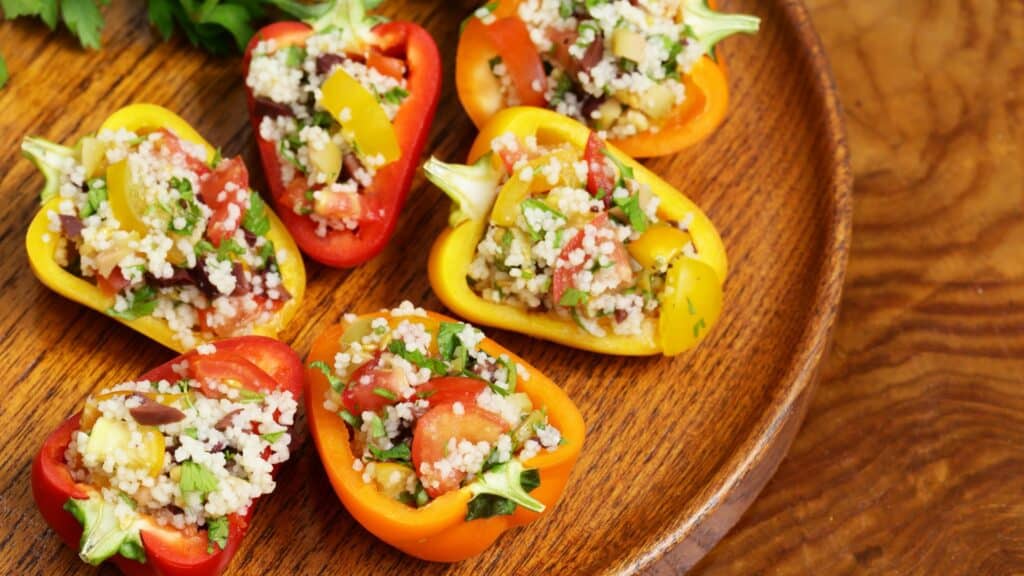 Colorful stuffed bell peppers with couscous on wooden plate
