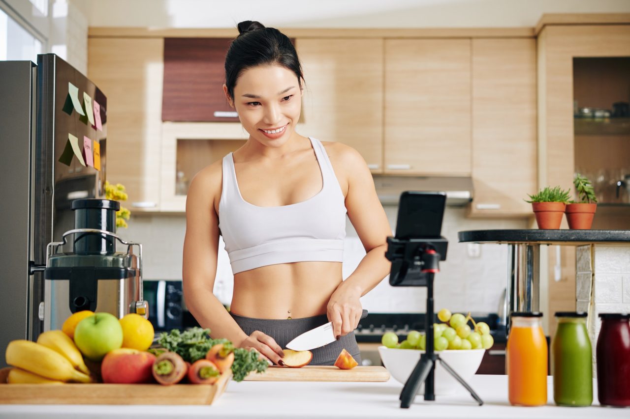 Woman recording cooking video in kitchen with fresh produce.