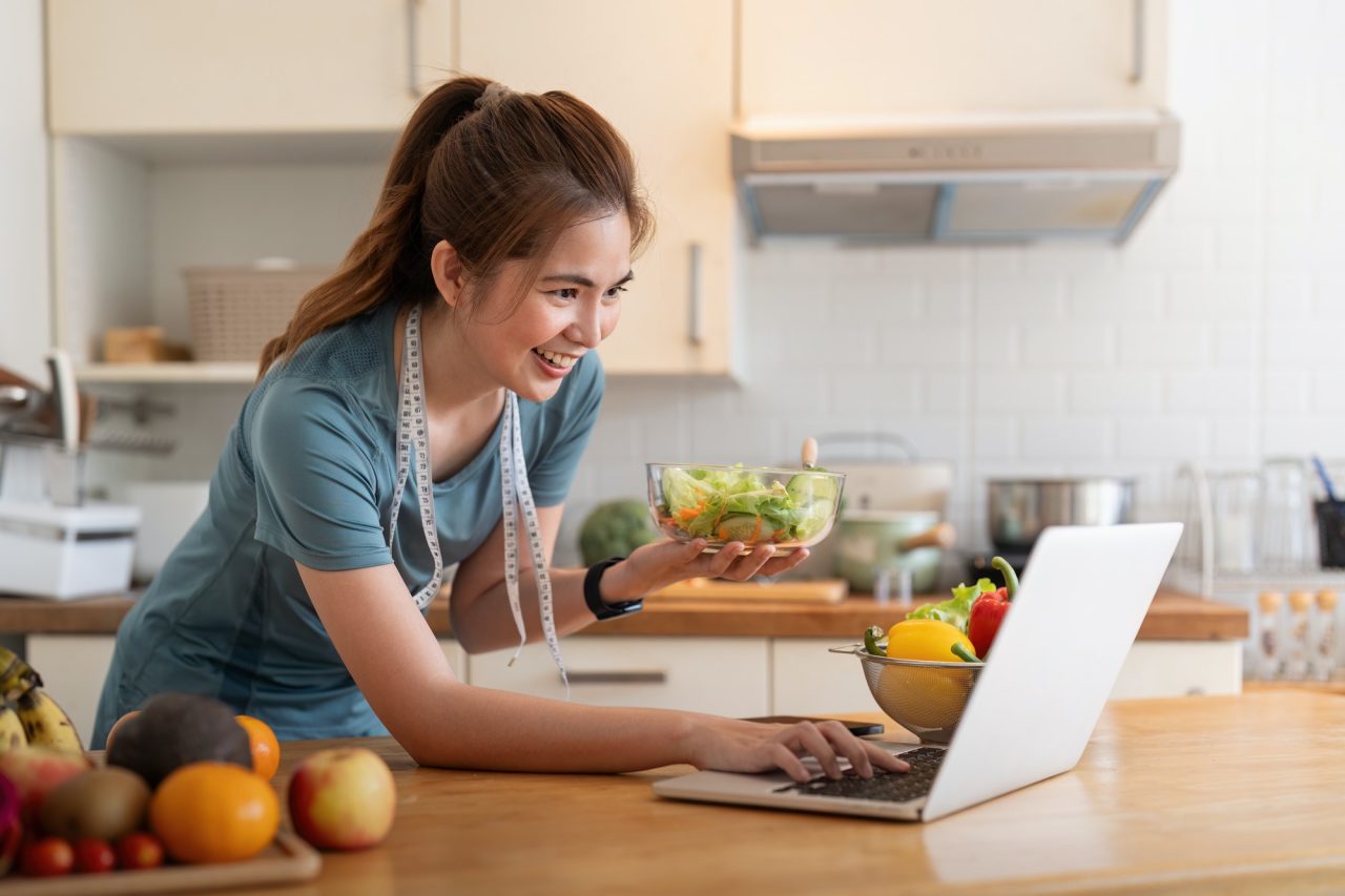 Woman preparing salad using laptop in kitchen.